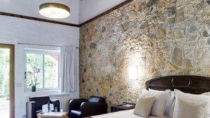 Ein Schlafzimmer mit Steinwand, einem Bett mit weißen Leinen, einem Holz-Kopfteil und einem Fenster mit Vorhängen.
