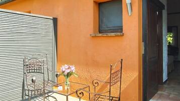 A patio with a metal table and chairs, a small window, and a door leading inside.