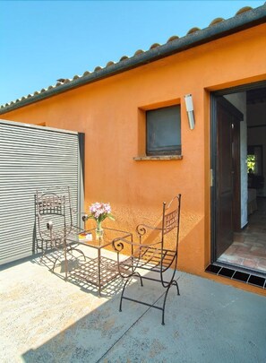A patio with a metal table and chairs, a small window, and a door leading inside. - Aatu (Forallac)