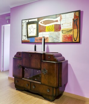 A wooden chest of drawers with a vase on top, set against a purple wall with a colorful abstract painting above. - Aatu (Forallac)