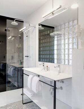 A modern bathroom with a glass shower enclosure, a large mirror with a mosaic backsplash, and a white vanity with a towel rack. - Aatu (Forallac)