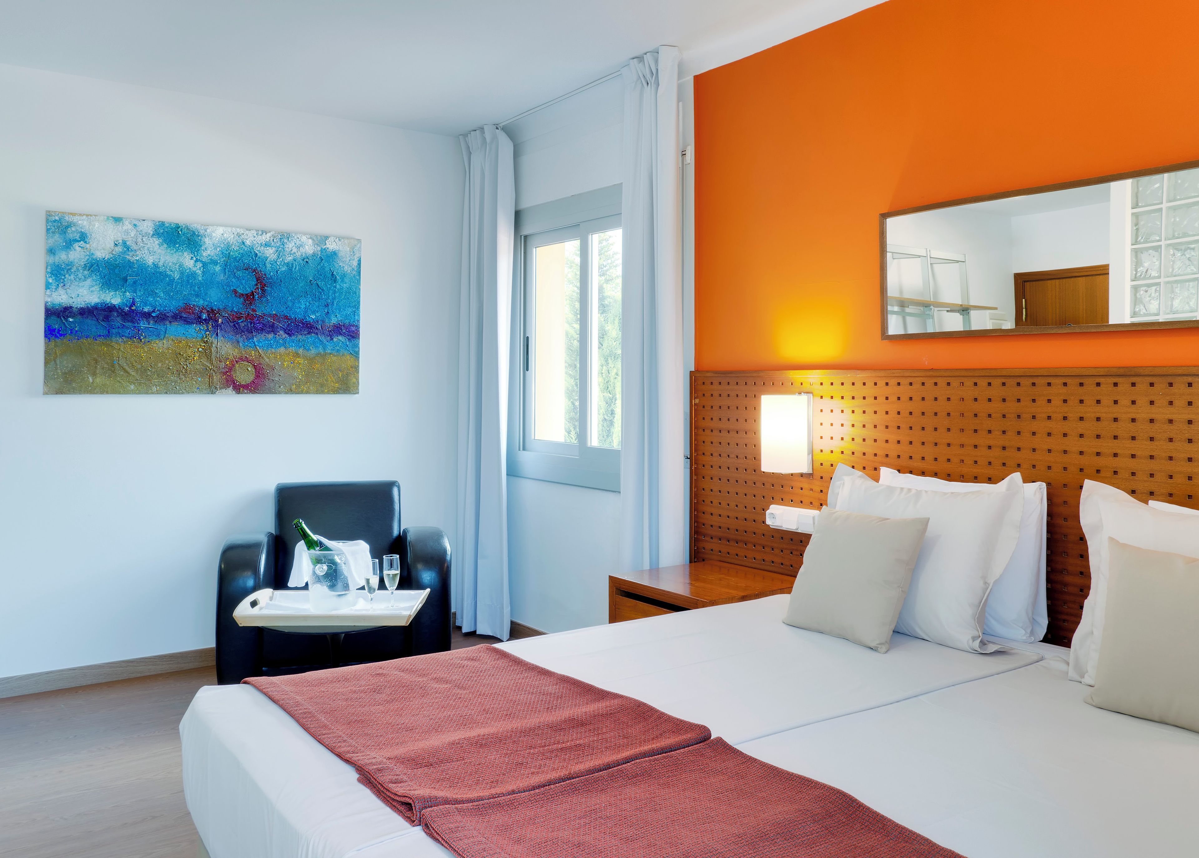 Una habitación de hotel con cama, un escritorio con silla, un cuadro y una ventana.