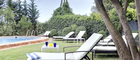 Un área junto a la piscina con sillones reclinables y una mesita con bebidas.