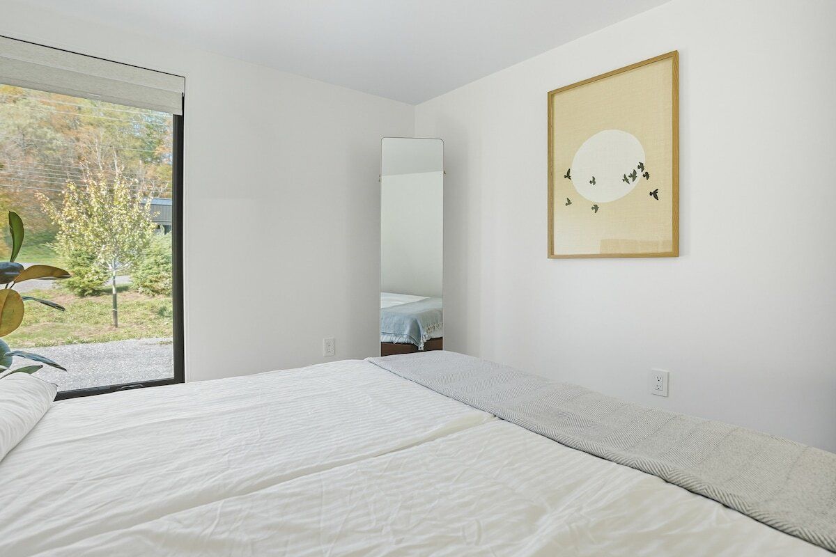 A bedroom with a bed, a window, a mirror, and a framed picture on the wall.
