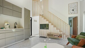 Una cocina moderna con estufa integrada, una zona de comedor con mesa y sillas blancas, y una escalera con barandilla de madera.
