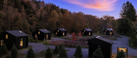 A row of cabins with a forest backdrop, a winding road, and a sign indicating the location.