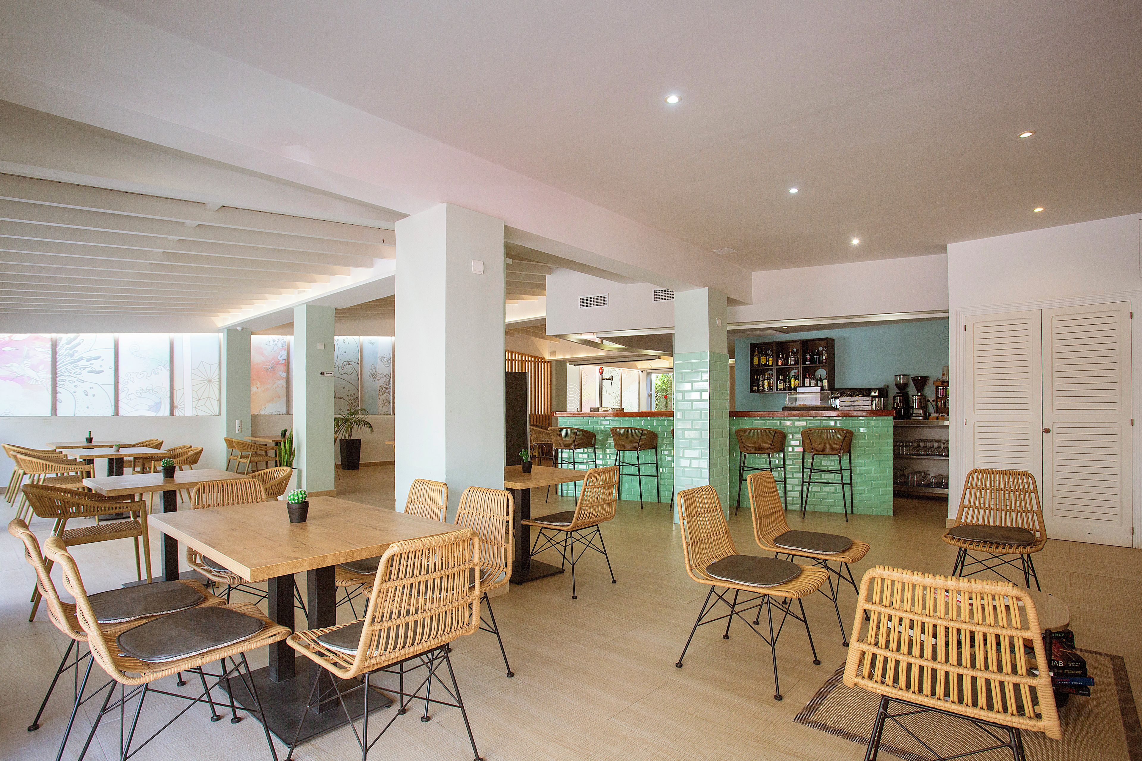 A spacious dining area with high tables and wicker chairs, a bar area with stools, and a view of the city through large windows.