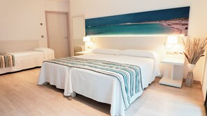 A hotel room with a large bed, two bedside tables with lamps, a small sofa, and a painting of a beach scene on the wall. - Hotel Rosales Formentera (Formentera)
