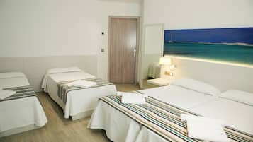 Habitación de hotel con tres camas, una puerta de madera, un cuadro de una playa y una lámpara de noche.