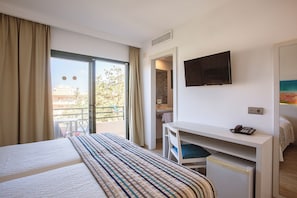 Habitación de hotel con cama, escritorio con silla, televisor y baño visible a través de una puerta abierta.