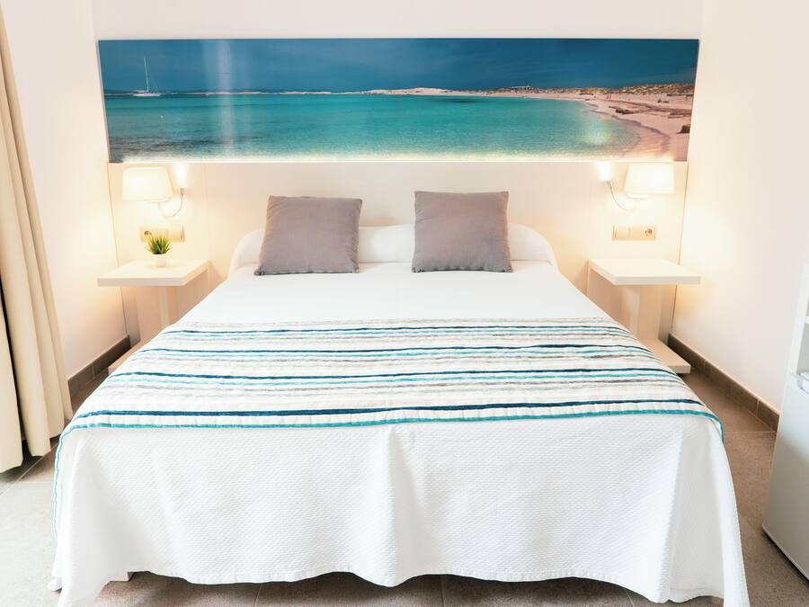 Een hotelkamer met een bed, twee bedlampen, een nachtkastje, een raam met gordijnen en een aan de muur bevestigde televisie.