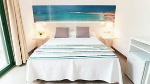 A hotel room with a bed, two bedside lamps, a nightstand, a window with curtains, and a wall-mounted TV. - Hotel Rosales Formentera (Formentera)