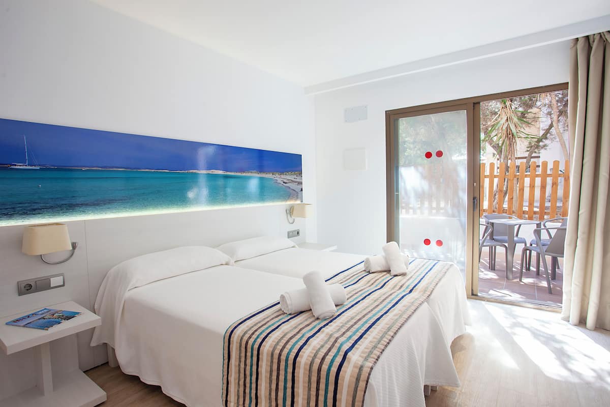Une chambre d’hôtel avec deux lits, une grande fenêtre donnant sur la mer et un balcon avec des sièges extérieurs.