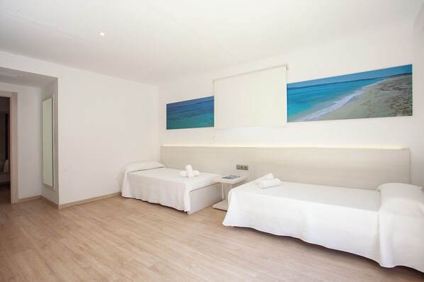 A hotel room with two single beds, a small table, and a wall-mounted TV. - Hotel Rosales Formentera (Formentera)