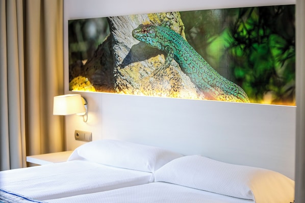 A hotel room with a bed, a wall-mounted lamp, and a framed picture of a lizard on the wall. - Hotel Rosales Formentera (Formentera)
