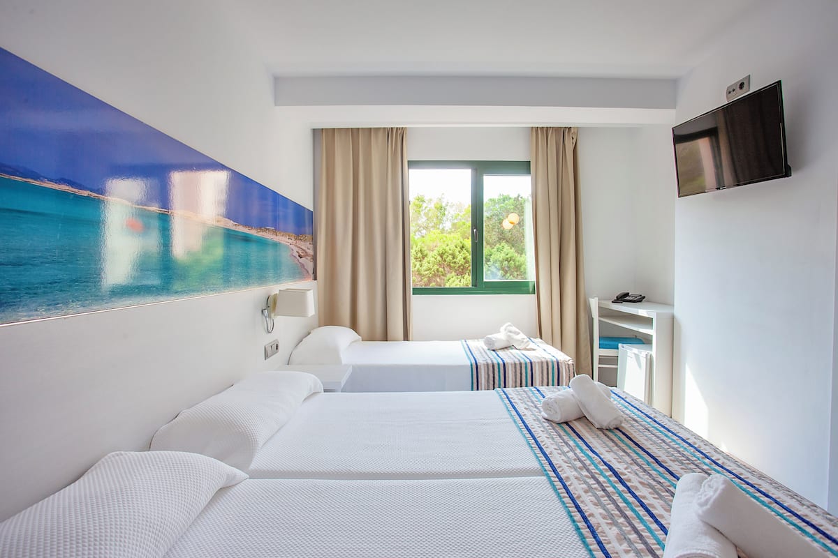 Une chambre d’hôtel avec deux lits, une télévision, un bureau et une fenêtre avec des rideaux.