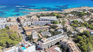 Luftaufnahme einer Küstenstadt mit Häusern, einem Strand und klarem, blauem Wasser.