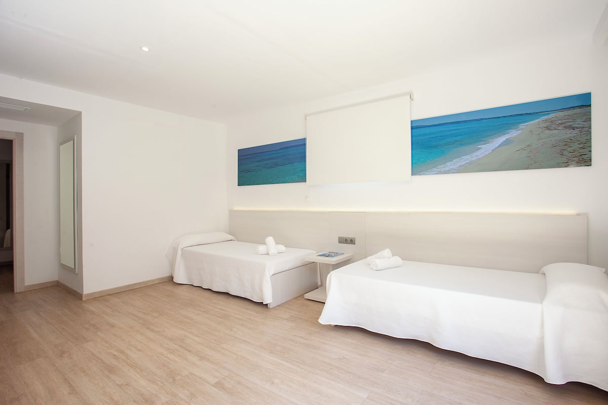 Une chambre d’hôtel avec deux lits simples, une petite table et un téléviseur fixé au mur.