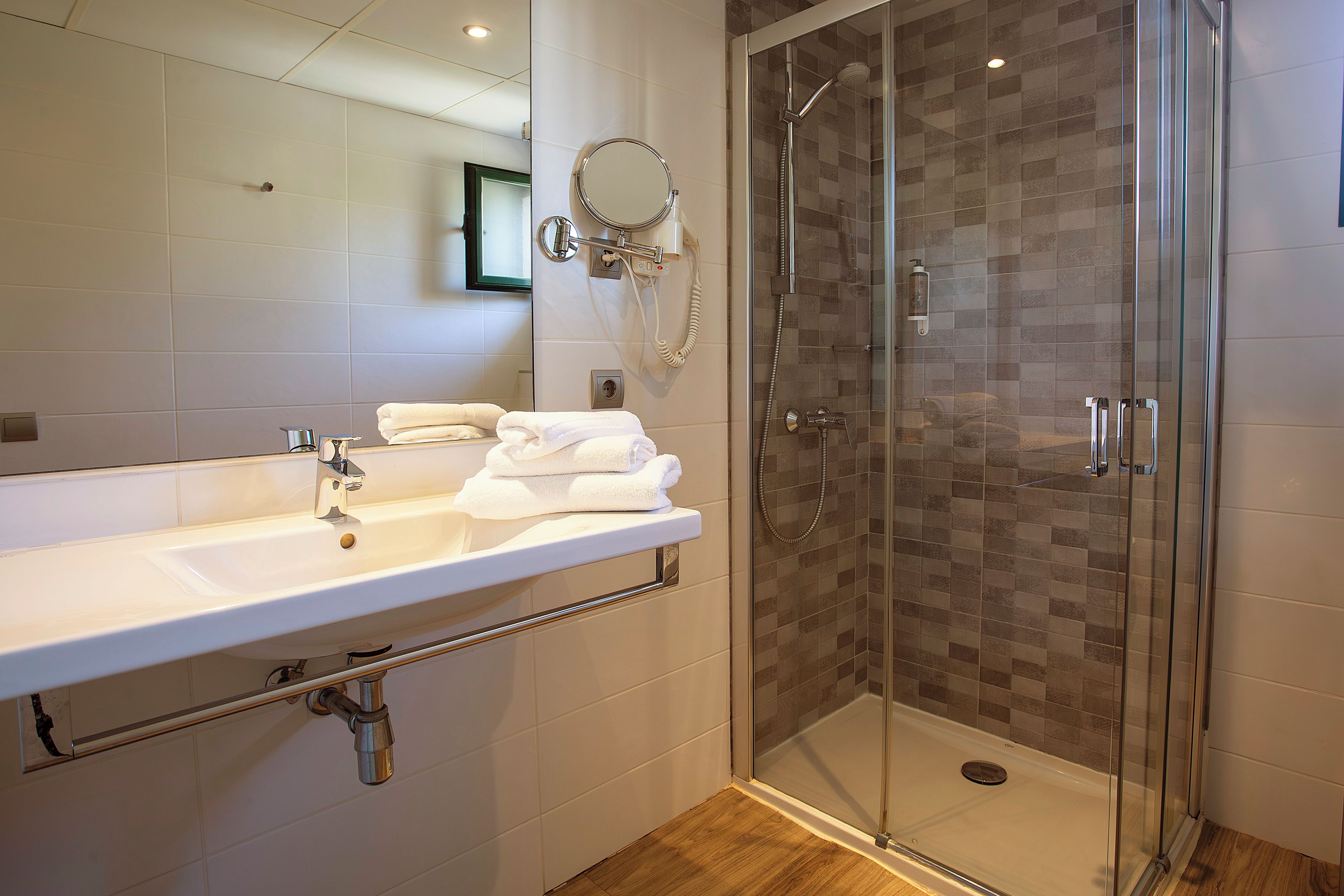 Un baño moderno con un lavabo blanco, una ducha con cerramiento de vidrio y un espejo sobre el lavabo.