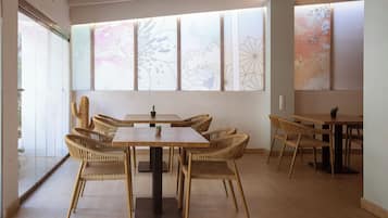 A dining area with a wooden table and wicker chairs, large windows with decorative patterns, and a light-colored floor.