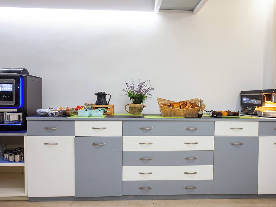 Una kitchenette con una cafetera, un hervidor, una cesta de pan y un jarrón con flores.
