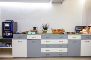 A kitchenette with a coffee machine, a kettle, a basket of bread, and a vase of flowers. - Hotel Rosales Formentera (Formentera)