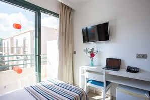 Ett hotellrum med en säng, ett skrivbord med en bärbar dator och en telefon, en tv på väggen och utsikt över byggnader utanför.
