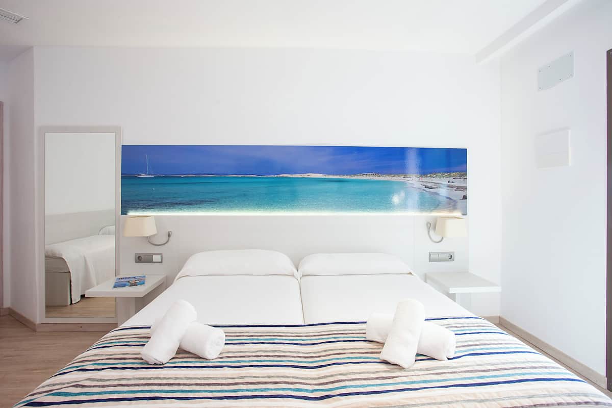Une chambre d’hôtel avec un grand lit, deux tables de chevet, une petite table et un tableau représentant une scène de plage.