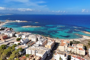 A coastal town with buildings along the beachfront, clear blue sea, and rocky outcrops. - Hotel Rosales Formentera (Formentera)