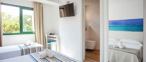 A hotel room with two beds, a TV, a bathroom, and a view of the sea.