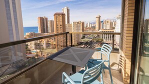 Un balcon avec une table et des chaises, donnant sur un paysage urbain avec de hauts immeubles et une étendue d’eau.