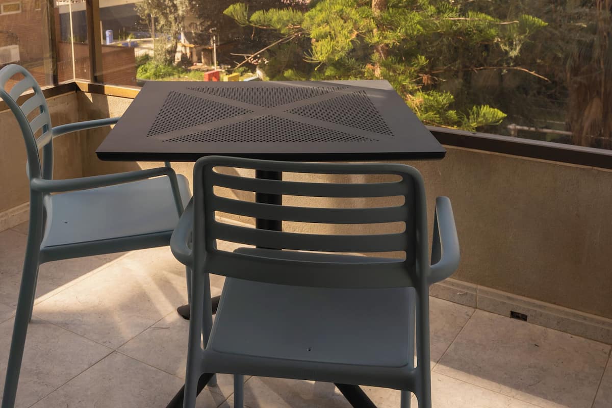 Un balcón con dos sillas y una mesa, con vista a un paisaje urbano con edificios altos y un árbol.