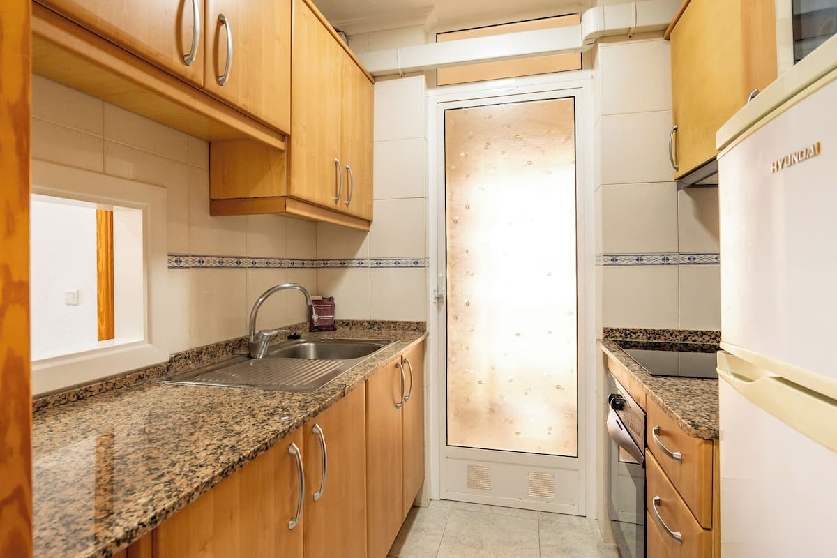 Una cocina con armarios de madera, encimeras de granito, un lavamanos de acero inoxidable y un refrigerador blanco.