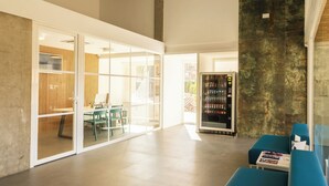 Un hall d’entrée spacieux au design moderne, comprenant un espace détente avec des canapés bleus, un distributeur automatique et une cloison en verre.