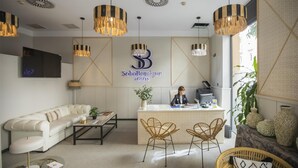 Een hotel receptie met een bank, twee rieten stoelen, een receptiebalie en een groot logo aan de muur.