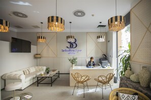 Ein Hotel-Empfangsbereich mit einer Couch, zwei Korbstühlen, einem Empfangstresen und einem großen Logo an der Wand.