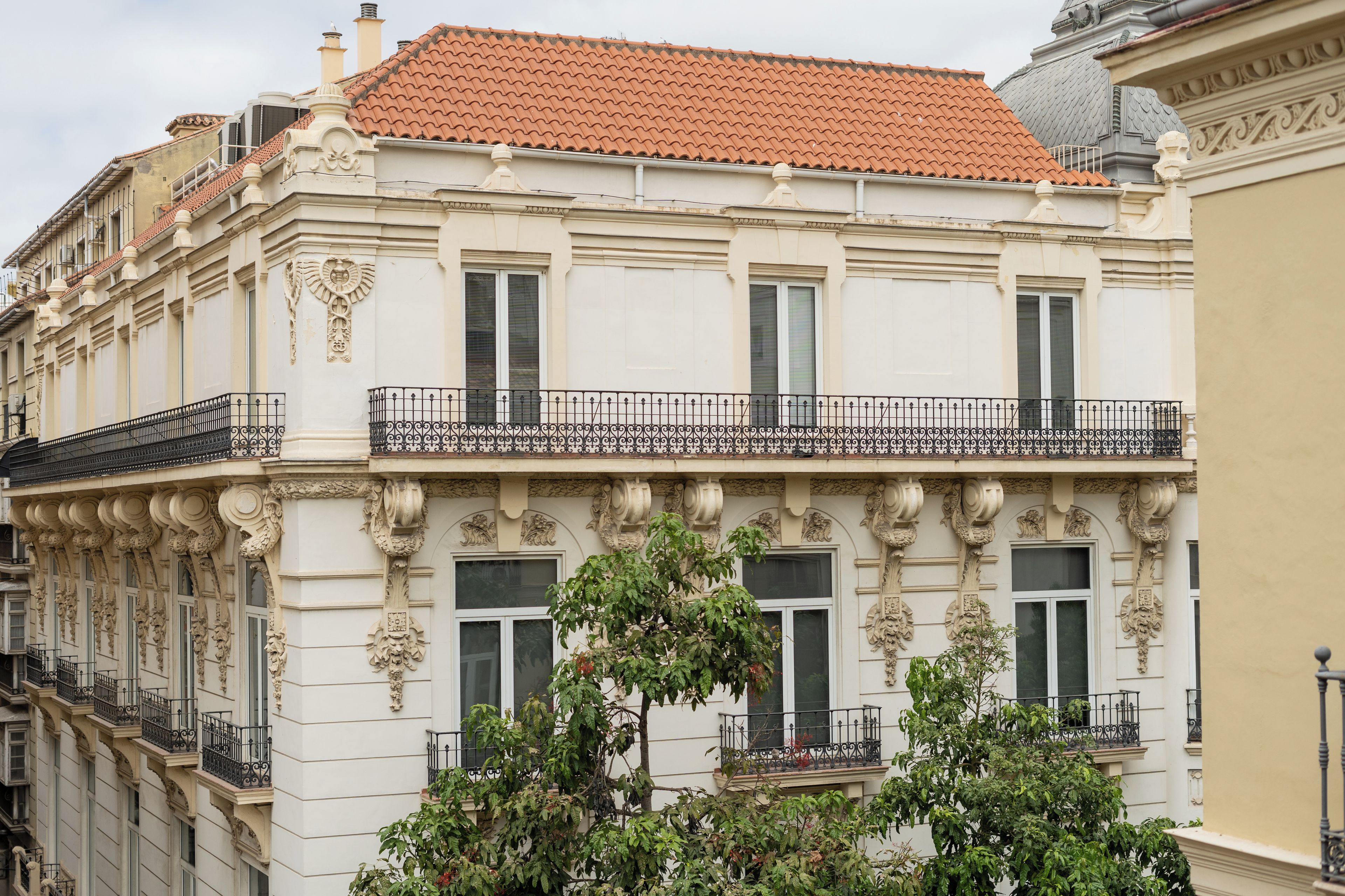 Ein Gebäude mit aufwendigen architektonischen Details, darunter dekorative Stuckarbeiten und ein Balkon mit schwarzen Geländern.