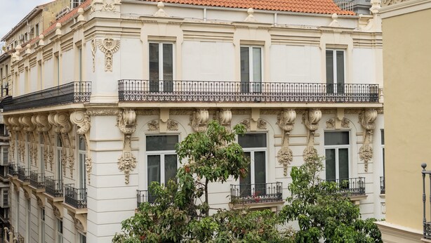 Een gebouw met versierde architecturale details, waaronder decoratieve sierlijsten en een balkon met zwarte leuningen.