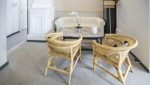 Ein Zimmer mit einem weißen Sofa, zwei Korbstühlen, einem Couchtisch und einer Topforchidee.