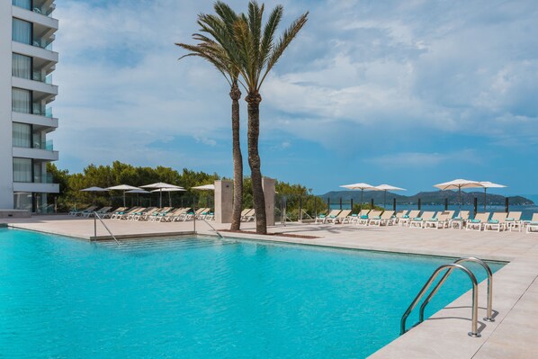 A swimming pool with lounge chairs and umbrellas, surrounded by palm trees and a modern building. - Iberostar Waves Cala Millor (Sant Llorenc des Cardassar)