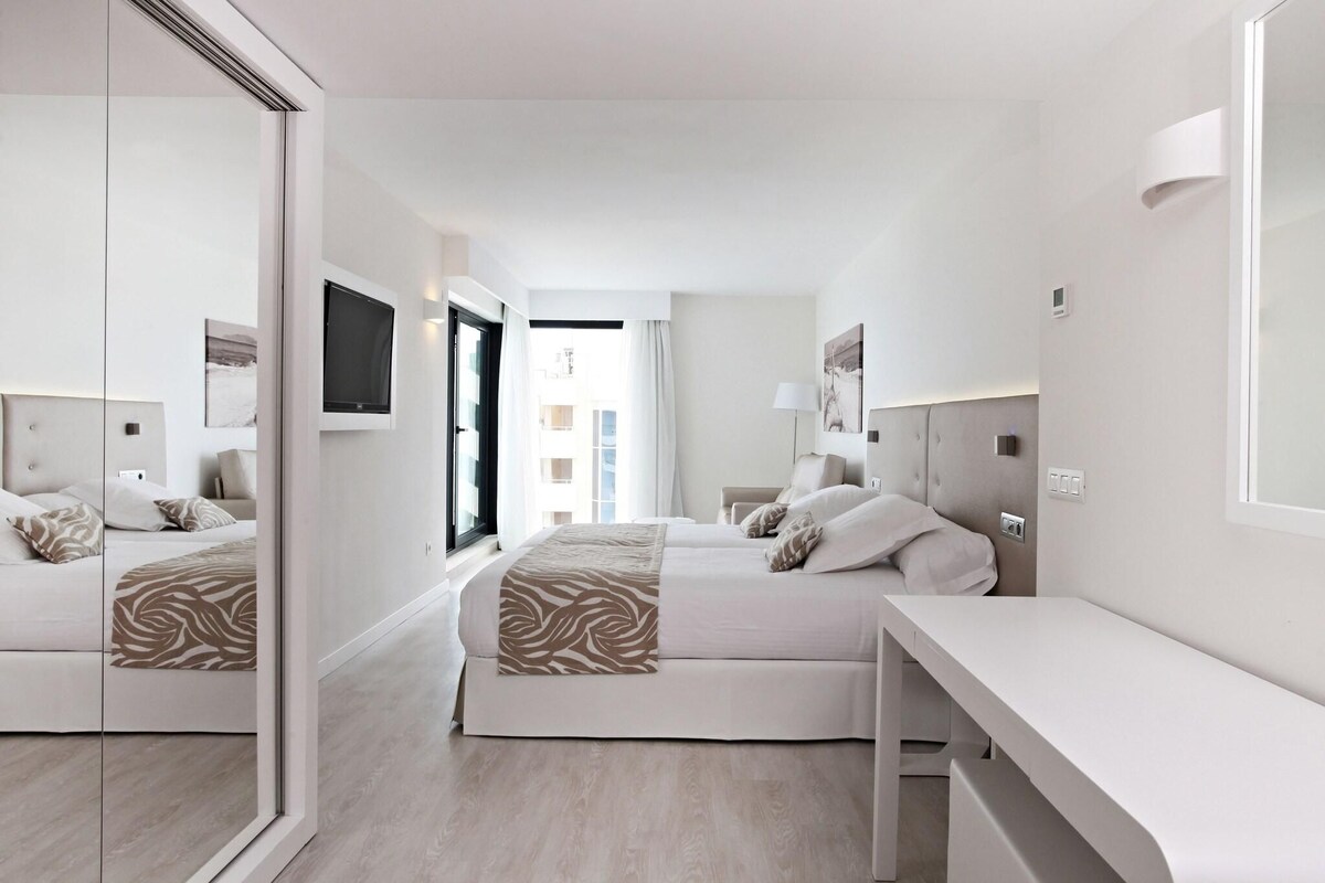A modern hotel room with two beds, a large mirror, and a desk.