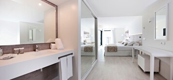 Un baño de hotel moderno con un espejo grande, un lavamanos y un perchero para toallas. La habitación tiene una cama con cabecero y una mesita de noche.