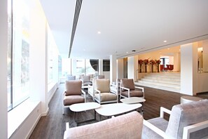 Eine moderne Lobby mit Sitzbereichen, einer Treppe und großen Fenstern.