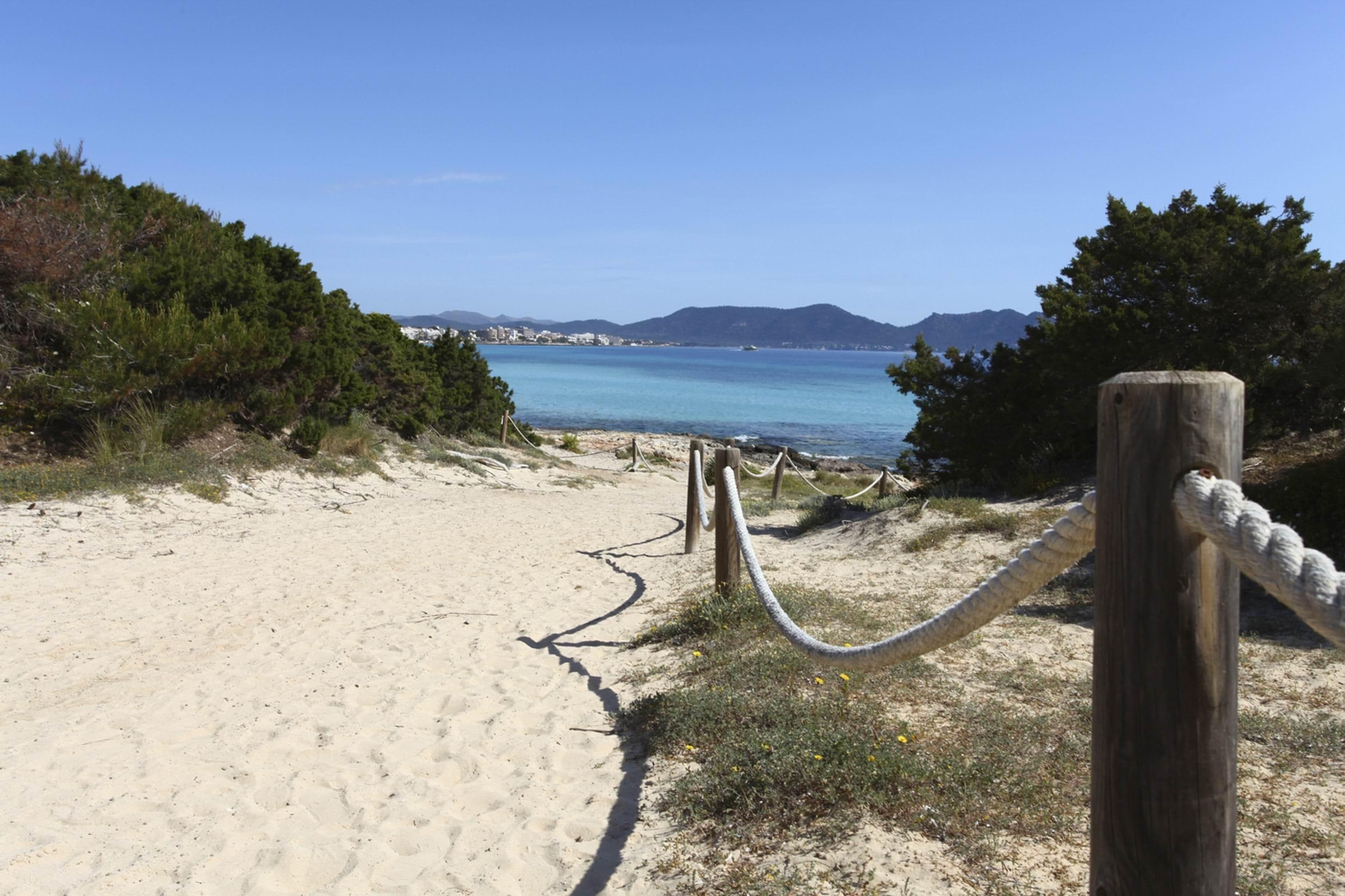 A sandy beach path leading to a body of water with a clear sky and distant mountains.