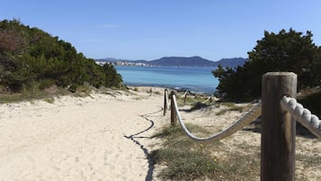 A sandy beach path leading to a body of water with a clear sky and distant mountains.