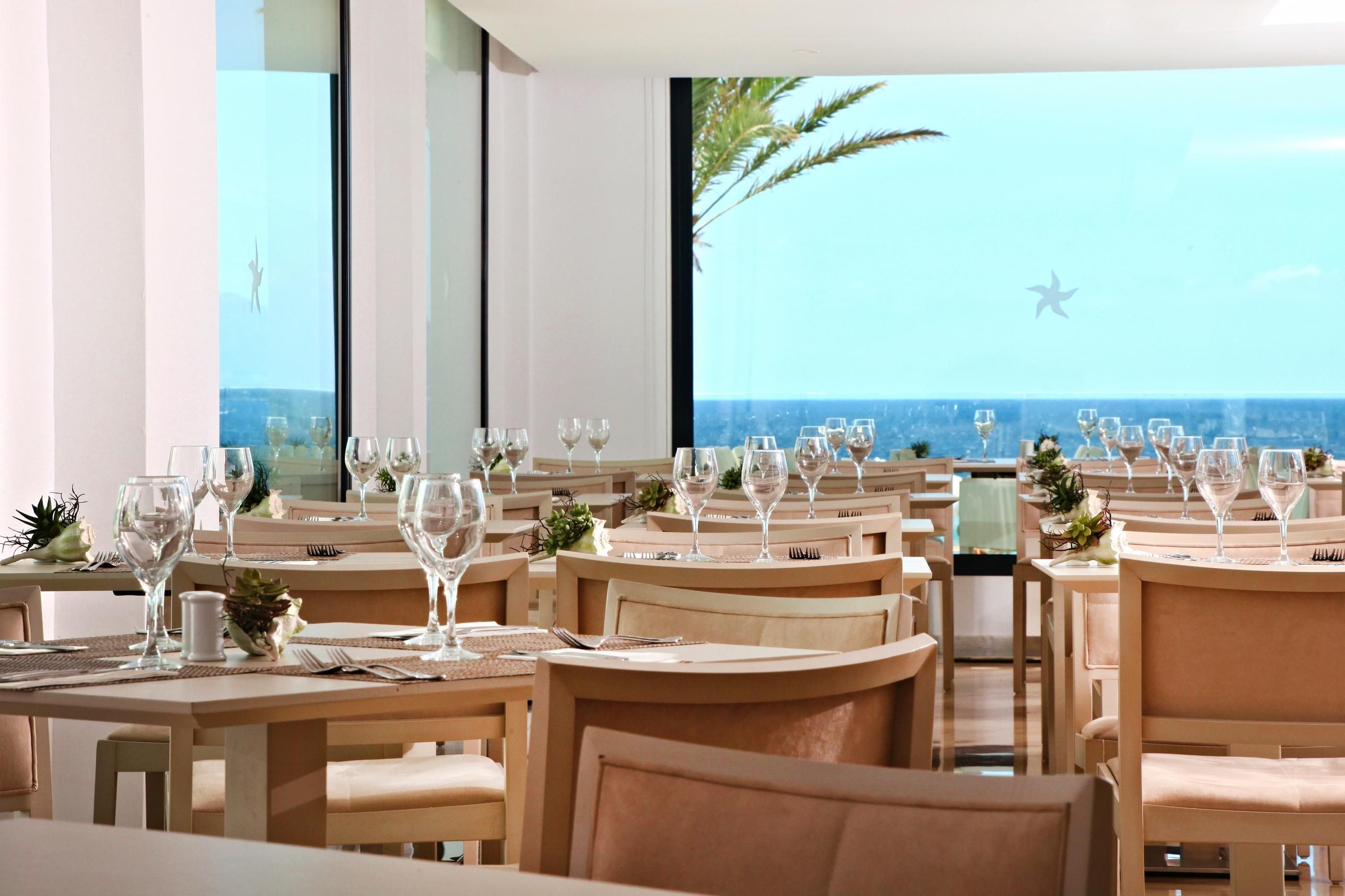 Een restaurant met gedekte tafels, met uitzicht op de oceaan en palmbomen.