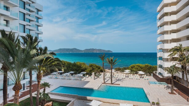 Ett modernt hotell med poolområde, palmer och utsikt över havet.
