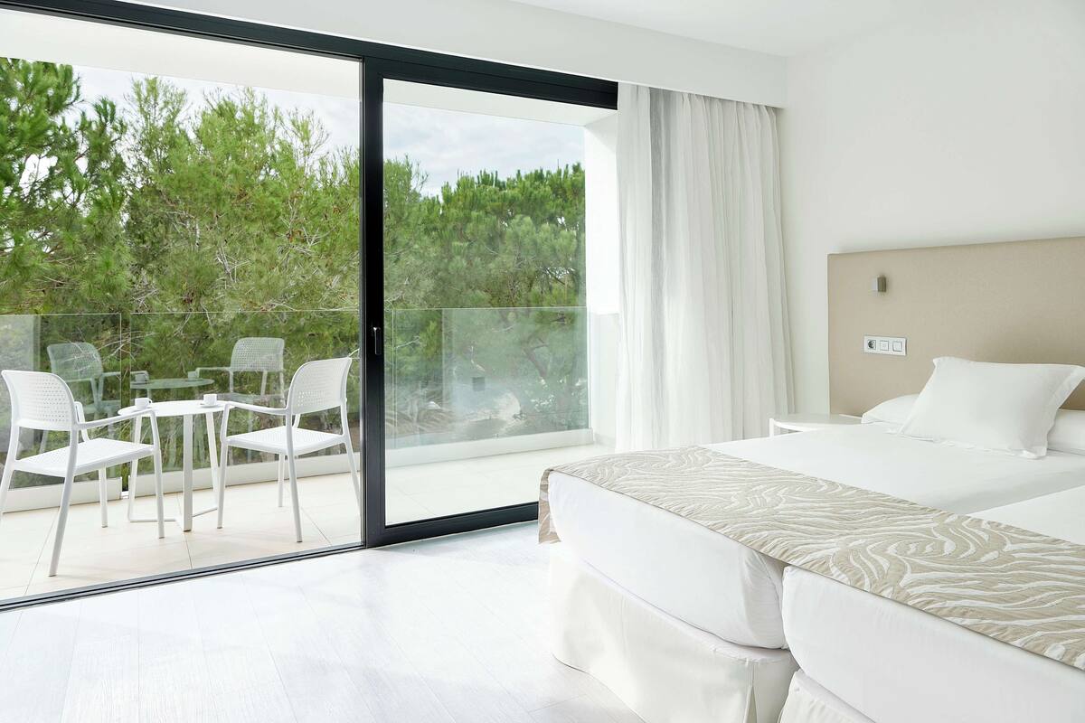 Quarto de hotel com cama, varanda com cadeiras e vista para árvores.