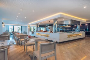 A modern restaurant with a central island, dining tables, and chairs. - Iberostar Waves Cala Millor (Sant Llorenc des Cardassar)