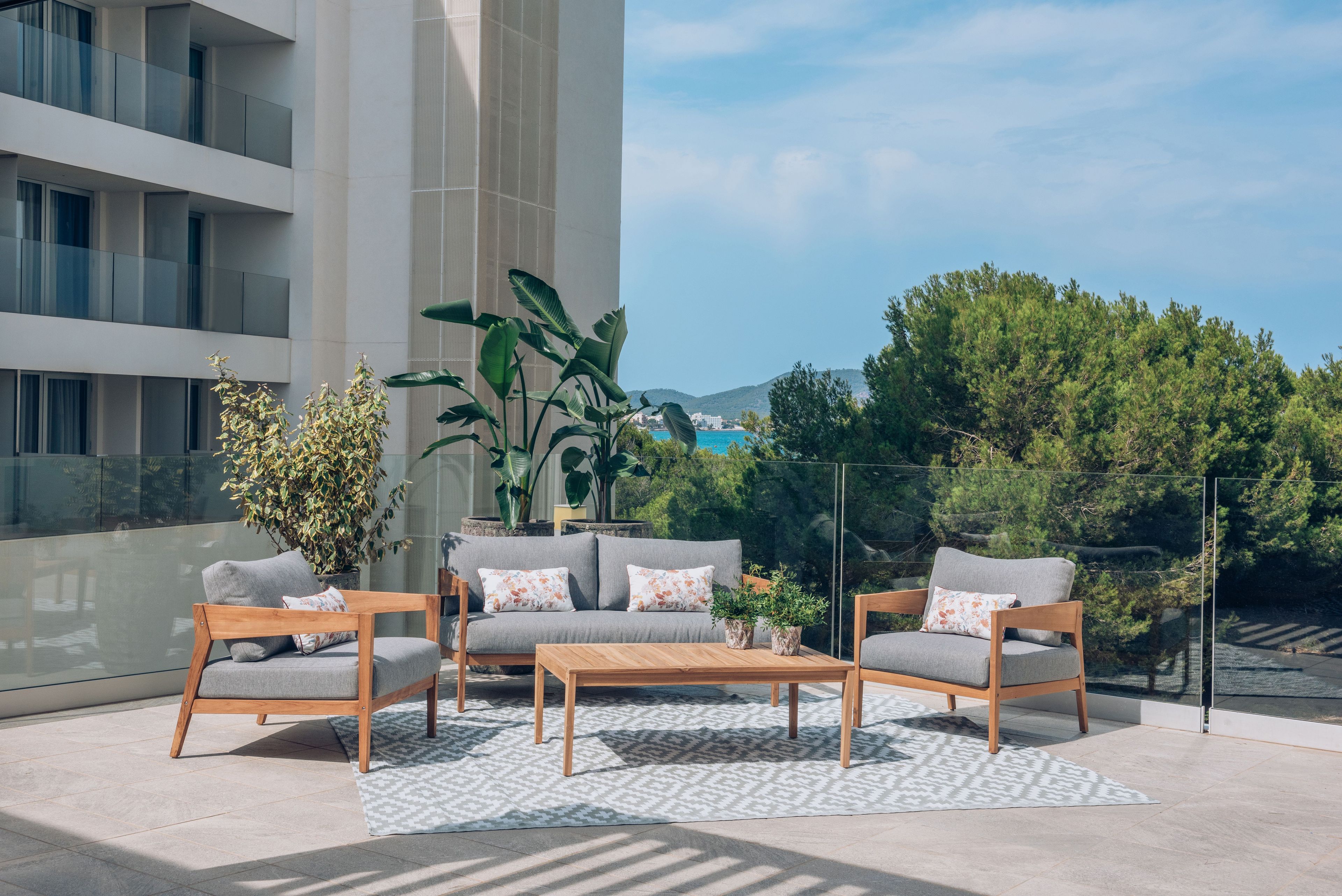 An outdoor seating area with a sofa and two chairs, a coffee table, and potted plants.